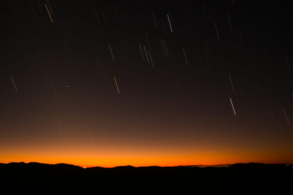 Meteorschauer: Sternschnuppen über Bergen bei Sonnenuntergang Meteorschauer am Nachthimmel mit Sternschnuppen über einer Bergsilhouette bei Sonnenuntergang